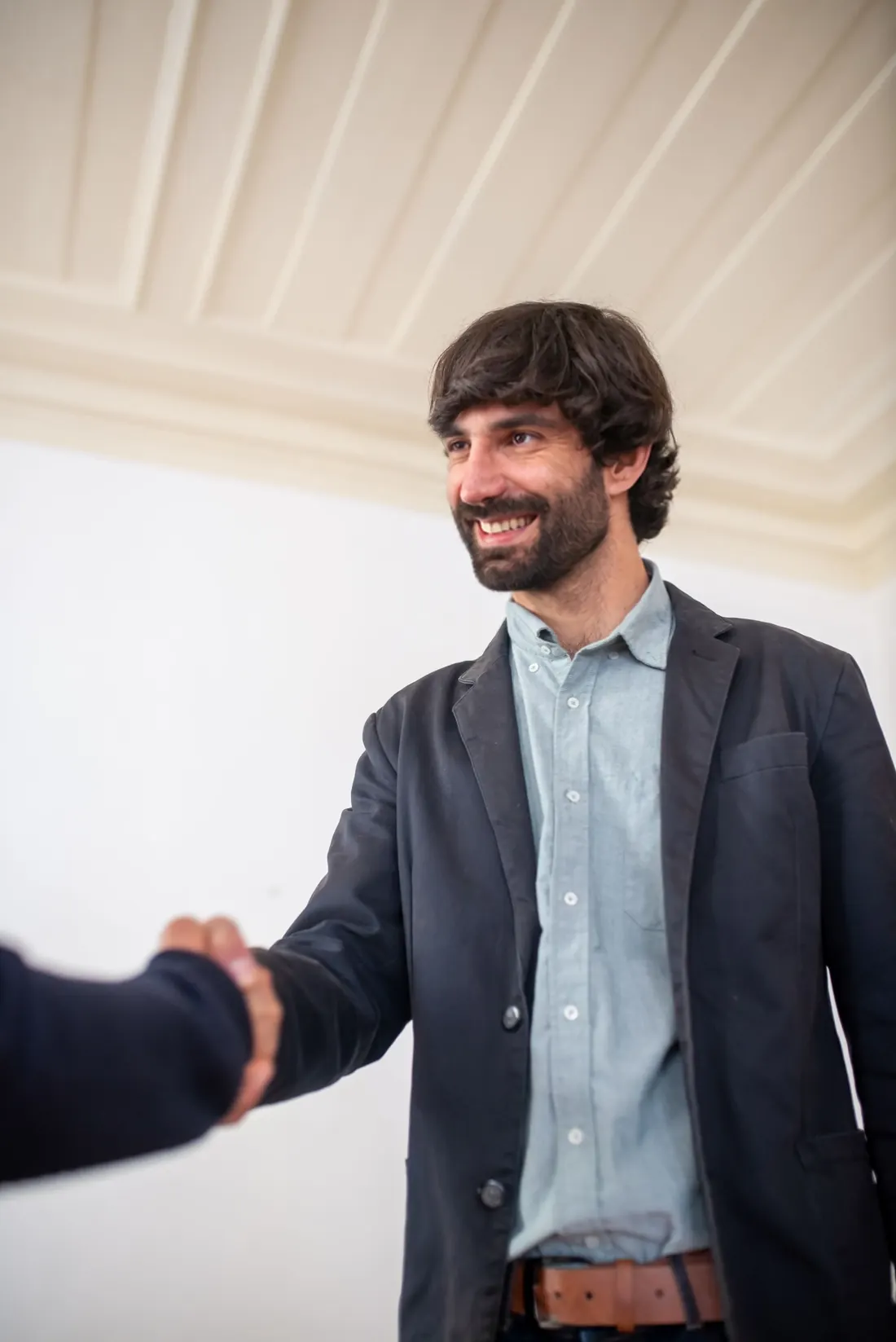 Un joven emprendedor sin corbata sonríe mientras da la mano a un nuevo cliente